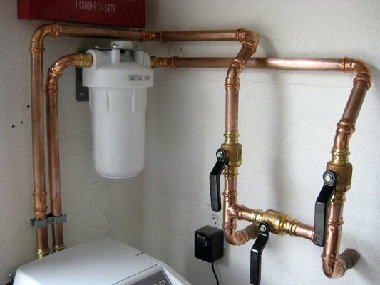 Copper plumbing system with a water filter on a white wall.